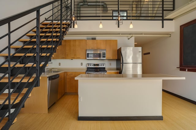 kitchen with stainless steel appliances, light wood-type flooring, a kitchen island, and a high ceiling