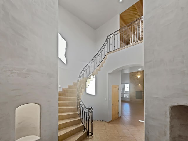 stairway with tile patterned floors, arched walkways, and a towering ceiling