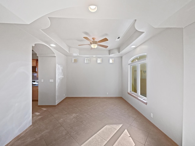 tiled empty room featuring ceiling fan and a tray ceiling