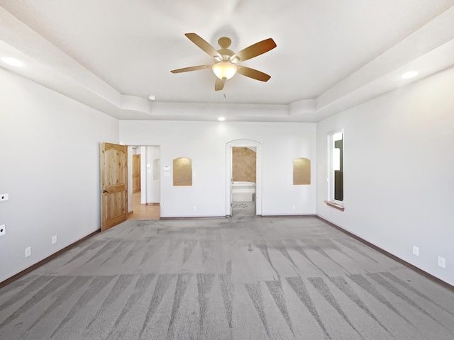 spare room featuring a raised ceiling, light carpet, and ceiling fan