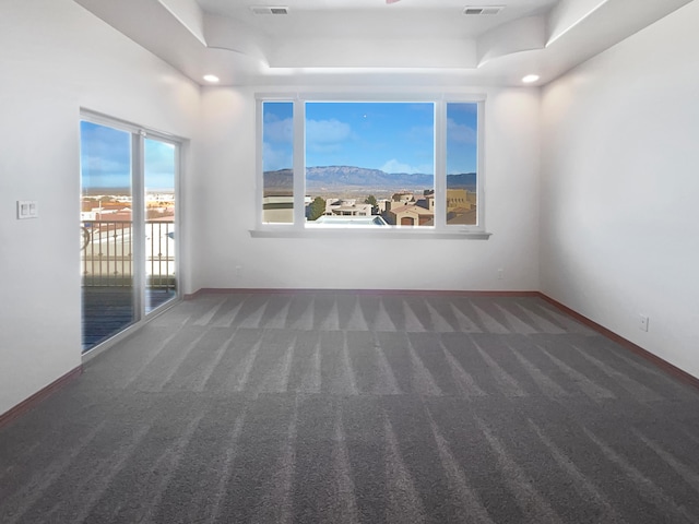 empty room with a mountain view, dark carpet, and a tray ceiling