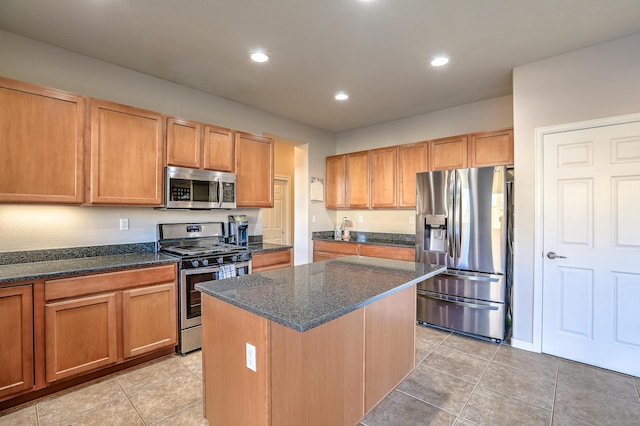 kitchen with light tile patterned flooring, appliances with stainless steel finishes, a kitchen island, and dark stone countertops