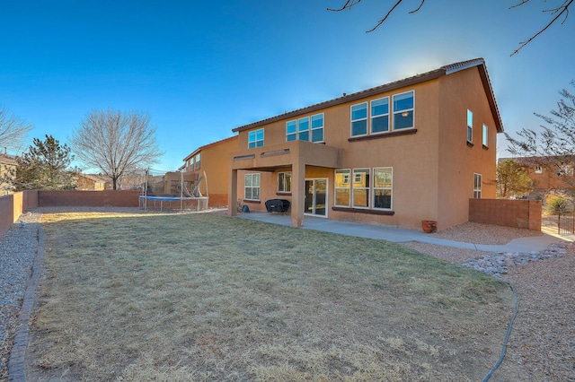 rear view of property featuring a patio area, a trampoline, and a lawn