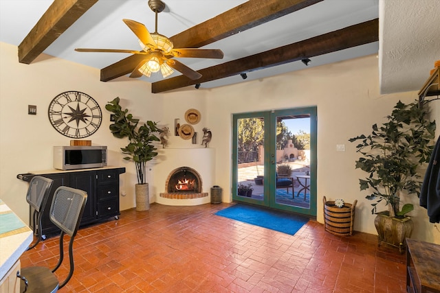 interior space featuring beamed ceiling, a brick fireplace, ceiling fan, and french doors