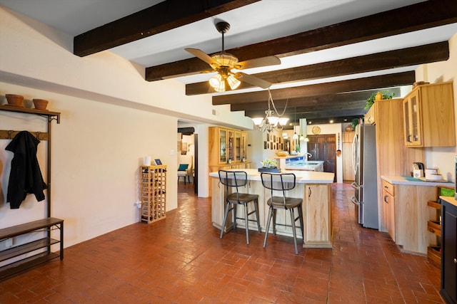 kitchen featuring a breakfast bar, ceiling fan with notable chandelier, stainless steel refrigerator, sink, and beam ceiling