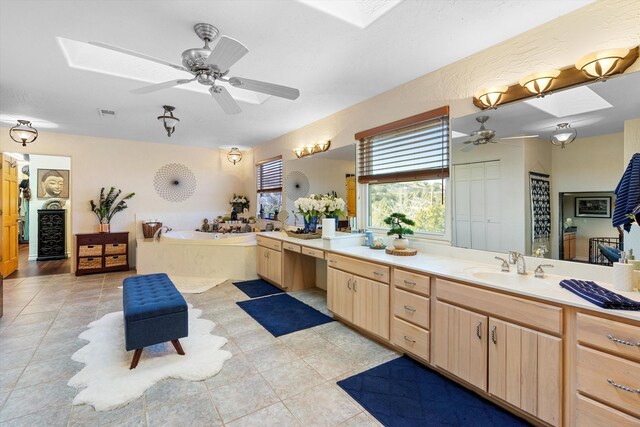 bathroom with a relaxing tiled tub, vanity, a skylight, and ceiling fan