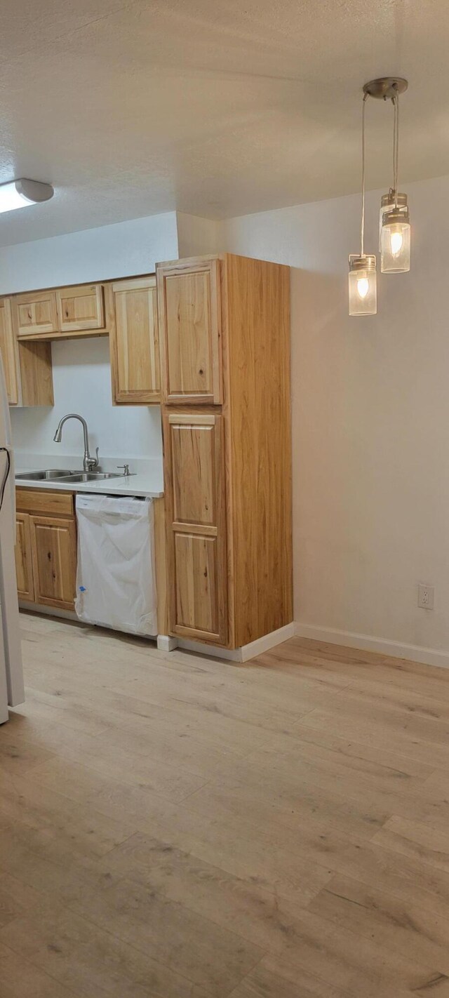 kitchen with sink, light hardwood / wood-style flooring, light brown cabinets, dishwasher, and pendant lighting