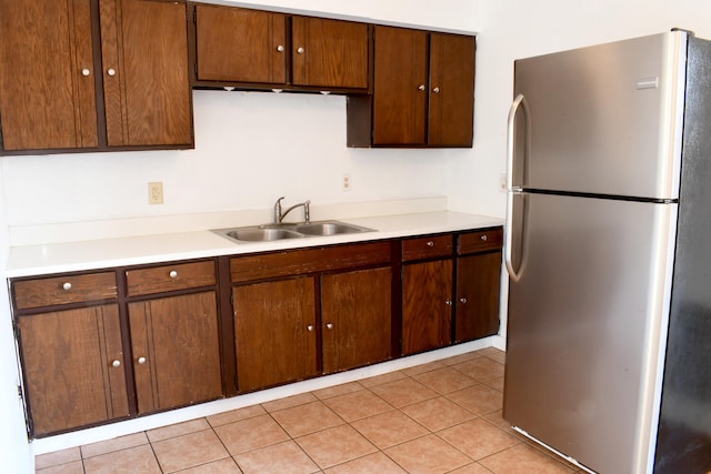 kitchen featuring stainless steel refrigerator, sink, dark brown cabinets, and light tile patterned floors