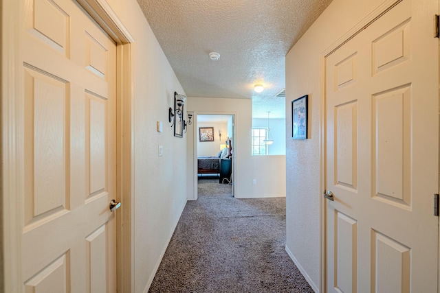 corridor featuring a textured ceiling and carpet flooring