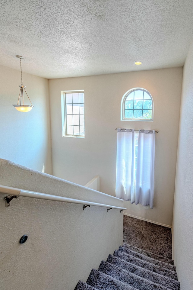 staircase featuring a textured ceiling, a healthy amount of sunlight, and carpet flooring