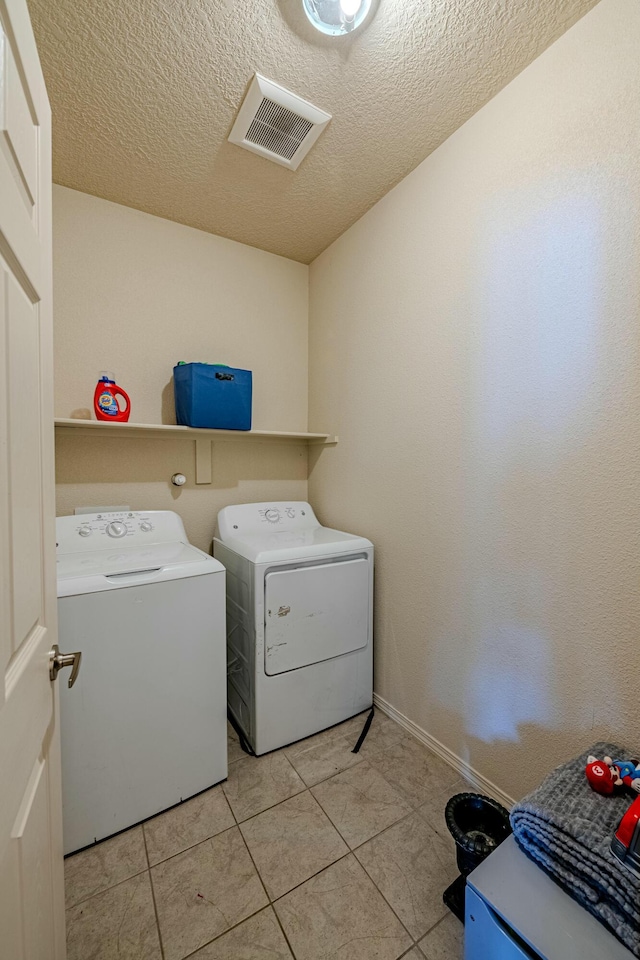 clothes washing area with washer and dryer, light tile patterned floors, and a textured ceiling