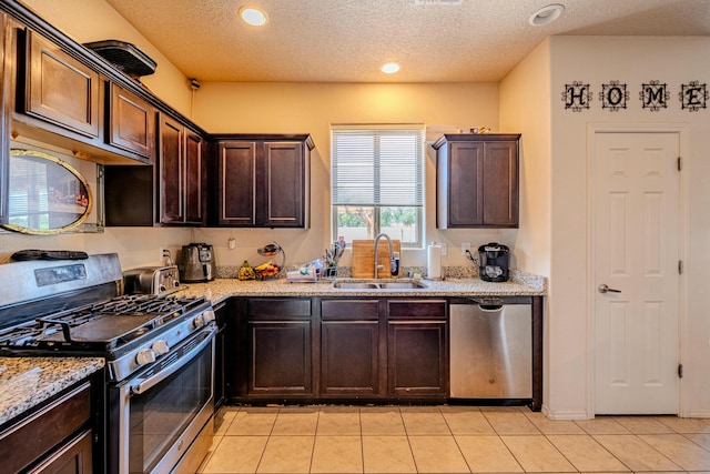 kitchen with sink, light tile patterned floors, light stone counters, dark brown cabinetry, and stainless steel appliances