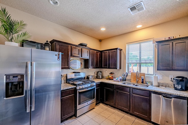 kitchen with sink, dark brown cabinets, light tile patterned floors, stainless steel appliances, and light stone countertops