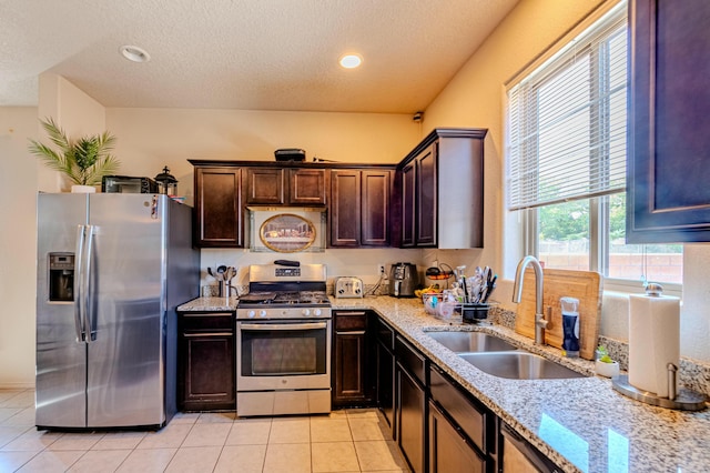 kitchen featuring sink, light tile patterned floors, stainless steel appliances, light stone counters, and a textured ceiling