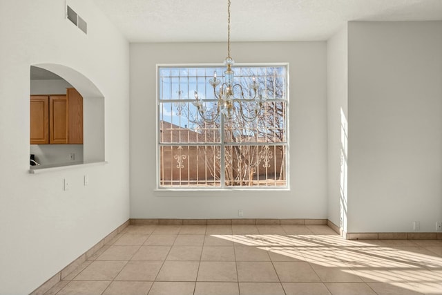 unfurnished dining area with a notable chandelier, a textured ceiling, and light tile patterned floors