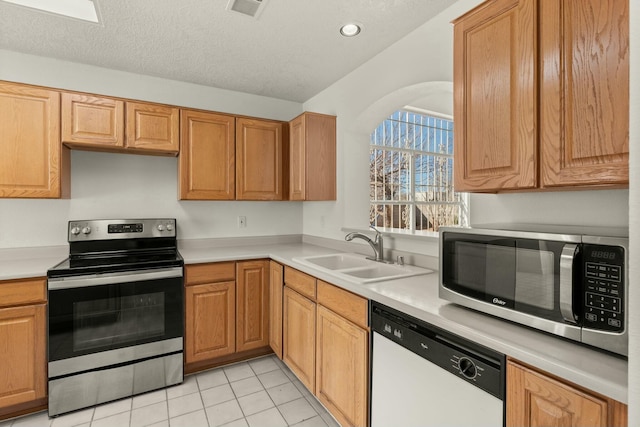 kitchen with appliances with stainless steel finishes, sink, light tile patterned floors, and a textured ceiling