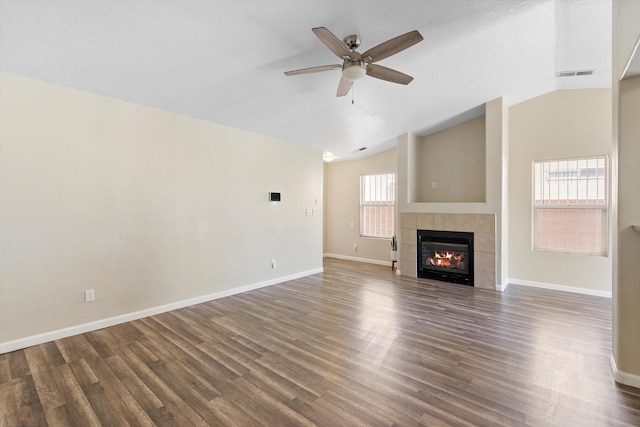 unfurnished living room with a tiled fireplace, dark wood-type flooring, ceiling fan, and vaulted ceiling