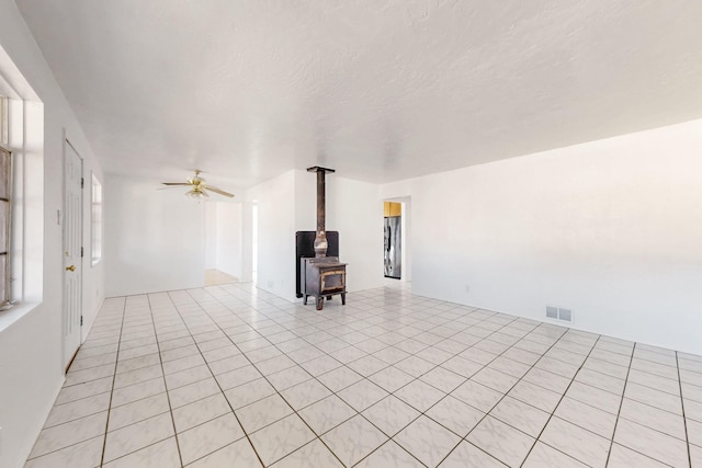 unfurnished living room with light tile patterned flooring, ceiling fan, a textured ceiling, and a wood stove