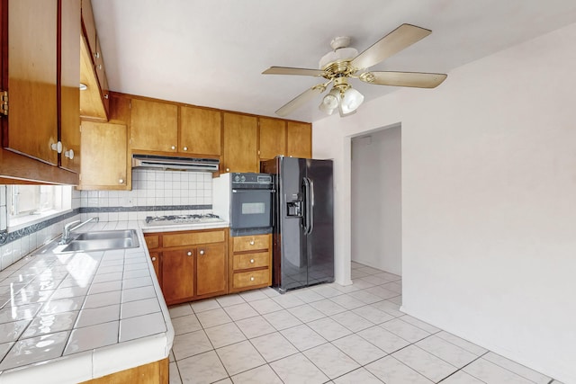 kitchen with sink, ceiling fan, tasteful backsplash, tile counters, and black appliances