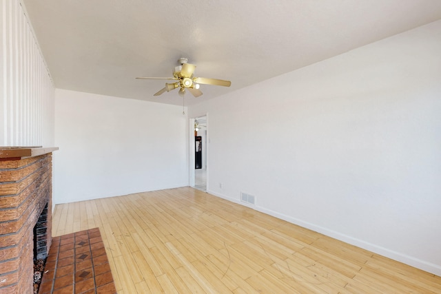 spare room with ceiling fan, wood-type flooring, and a brick fireplace