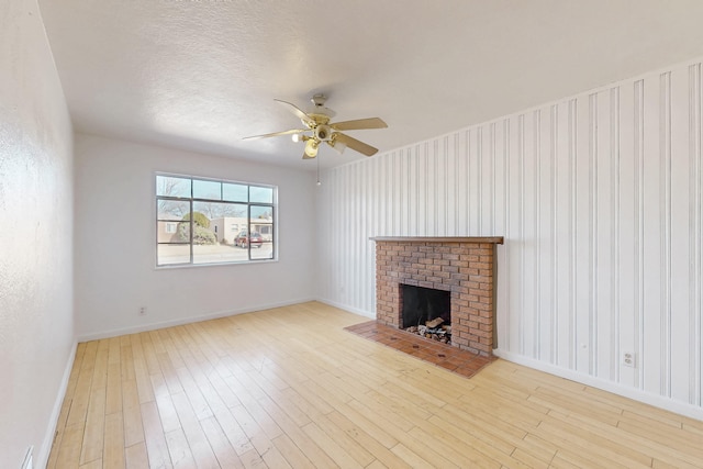 unfurnished living room featuring ceiling fan, light hardwood / wood-style floors, a brick fireplace, and a textured ceiling