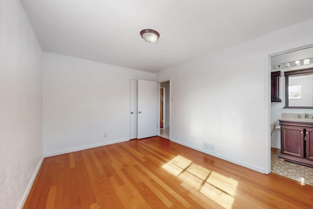 unfurnished bedroom with connected bathroom, sink, and light wood-type flooring