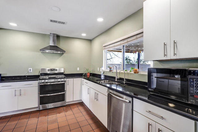 kitchen featuring sink, white cabinetry, appliances with stainless steel finishes, dark tile patterned floors, and wall chimney range hood