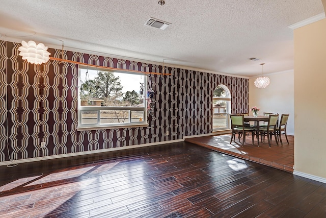 empty room featuring crown molding, hardwood / wood-style floors, a notable chandelier, and a wealth of natural light