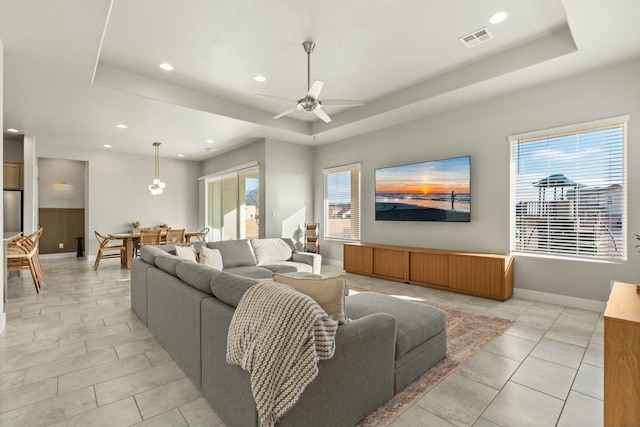 tiled living room with ceiling fan and a tray ceiling