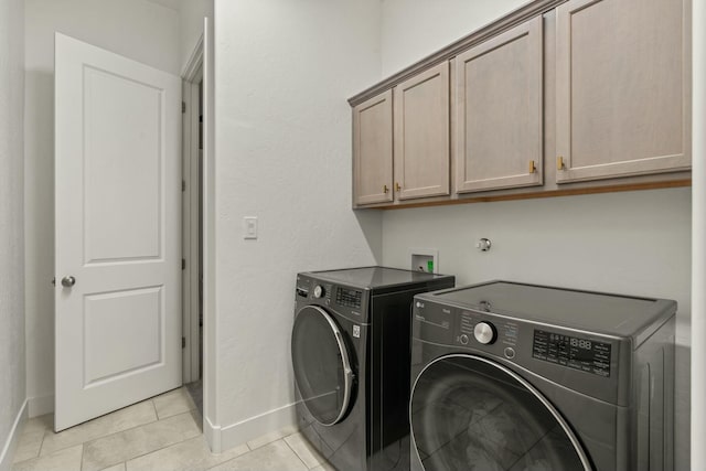 clothes washing area with light tile patterned floors, washing machine and dryer, and cabinets