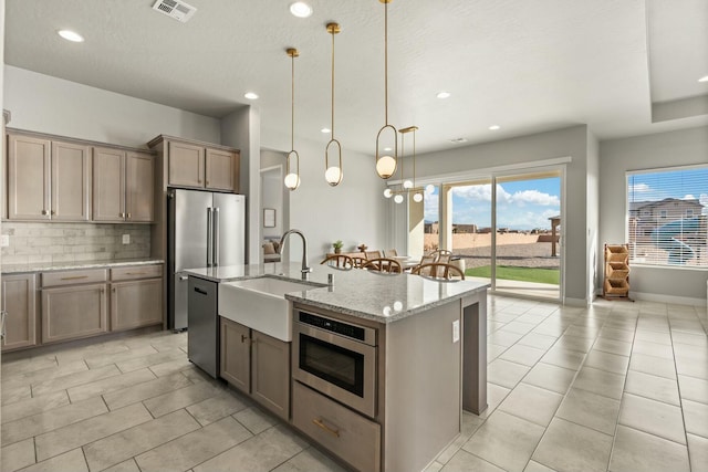 kitchen featuring decorative light fixtures, an island with sink, sink, stainless steel appliances, and light stone countertops