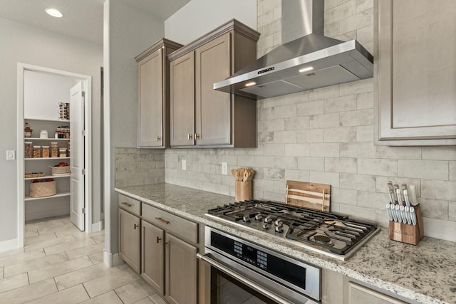 kitchen featuring tasteful backsplash, wall chimney range hood, stainless steel appliances, and light stone countertops