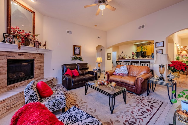 living room with lofted ceiling, a stone fireplace, and ceiling fan