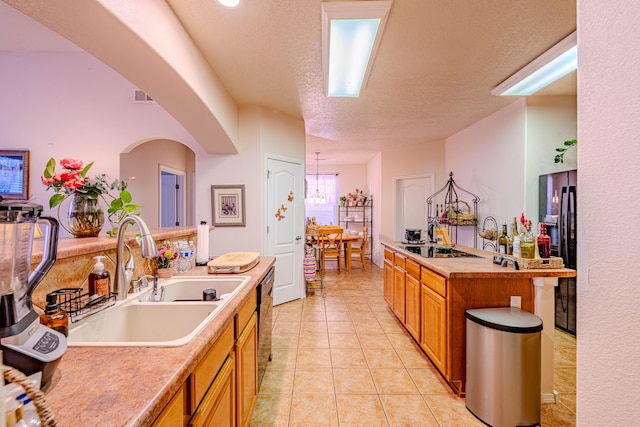 kitchen with an island with sink, sink, light tile patterned floors, black appliances, and a textured ceiling