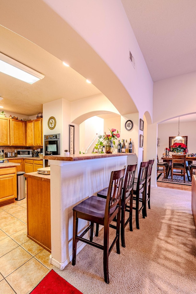 kitchen with light tile patterned floors, kitchen peninsula, and a kitchen bar