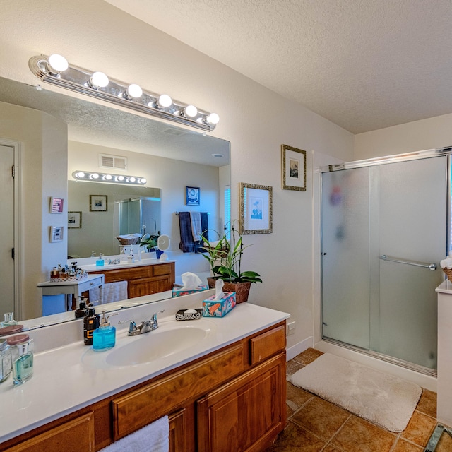 bathroom with tile patterned flooring, vanity, a shower with door, and a textured ceiling