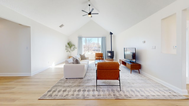 living room with high vaulted ceiling, light hardwood / wood-style floors, ceiling fan, and a wood stove