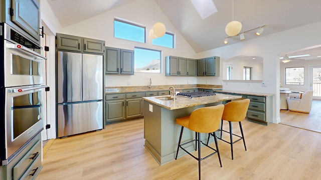 kitchen featuring sink, appliances with stainless steel finishes, a kitchen island with sink, light stone countertops, and decorative light fixtures