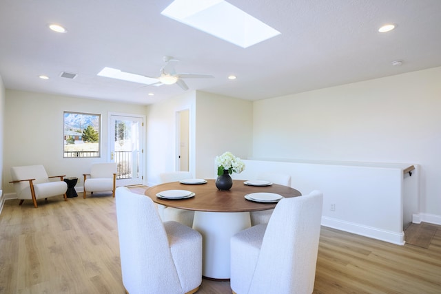 dining area with ceiling fan, a skylight, and light wood-type flooring