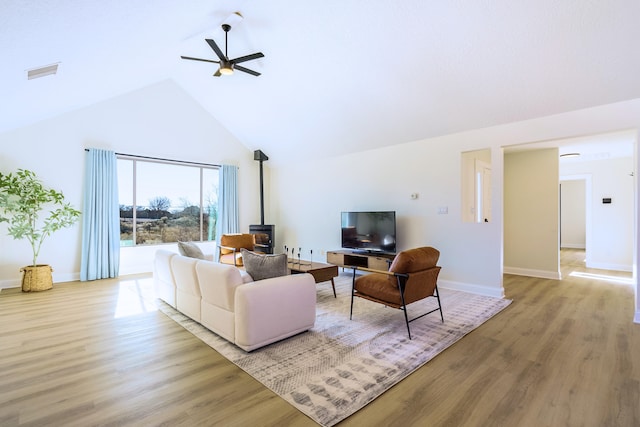 living room with ceiling fan, high vaulted ceiling, a wood stove, and light wood-type flooring