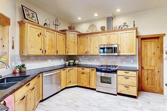 kitchen with sink, light hardwood / wood-style flooring, appliances with stainless steel finishes, decorative backsplash, and dark stone counters