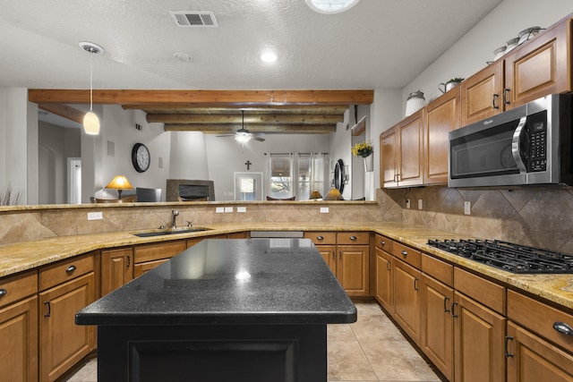 kitchen with sink, a kitchen island, beam ceiling, black gas stovetop, and backsplash