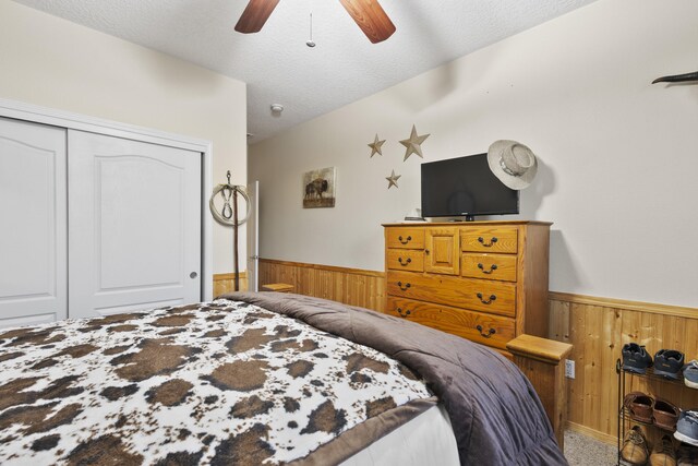 bedroom with ceiling fan, wooden walls, a closet, and a textured ceiling