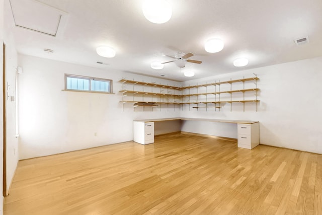 unfurnished office with built in desk, light hardwood / wood-style floors, and ceiling fan