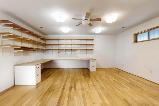 unfurnished office with ceiling fan, built in desk, and light wood-type flooring