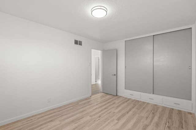 unfurnished bedroom with a closet, light hardwood / wood-style floors, and a textured ceiling