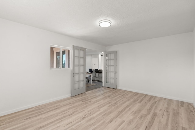 spare room featuring a textured ceiling, light hardwood / wood-style floors, and french doors