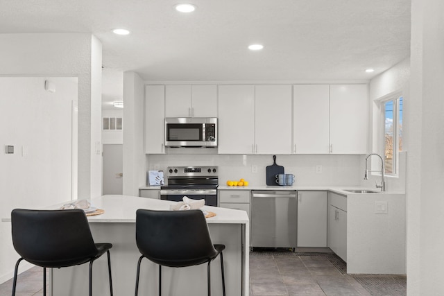 kitchen with sink, stainless steel appliances, a center island, white cabinets, and a kitchen bar