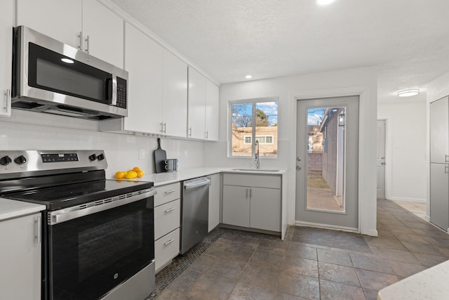 kitchen with sink, white cabinetry, a textured ceiling, appliances with stainless steel finishes, and backsplash