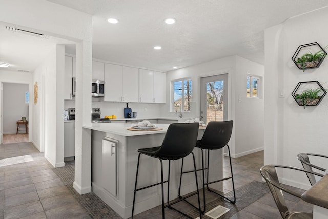 kitchen with a kitchen bar, sink, kitchen peninsula, stainless steel appliances, and white cabinets